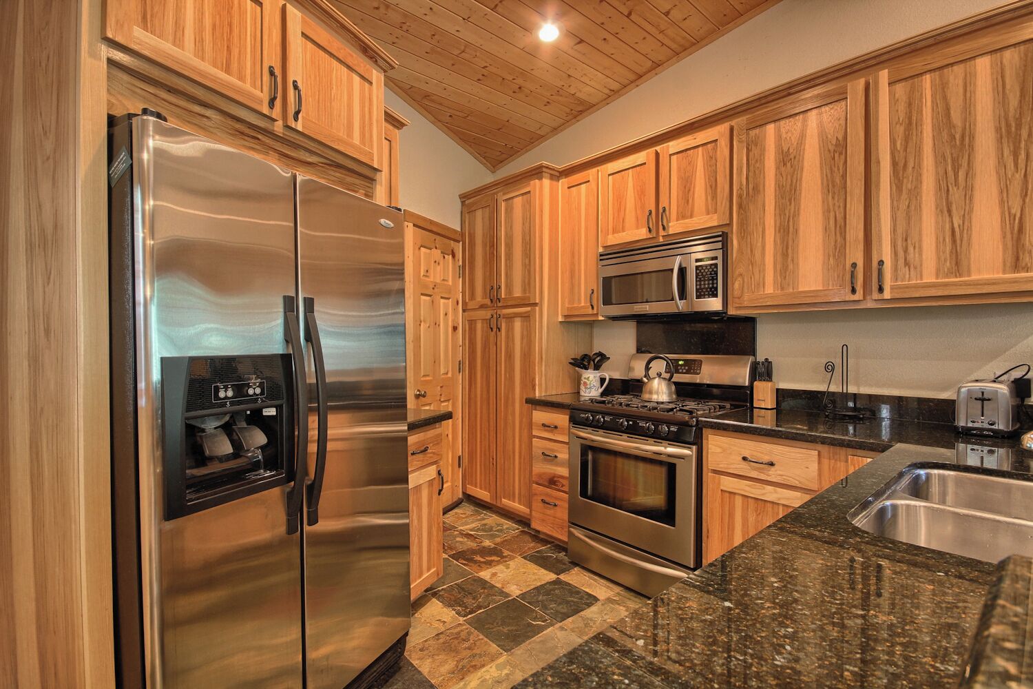 A kitchen with wooden cabinets, stainless steel appliances, granite countertops, and a checkered tile floor.