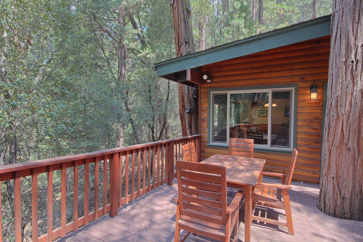 Une terrasse en bois, agrémentée d’une table et de chaises, entourée d’une balustrade en bois, et offrant une vue sur une zone boisée.