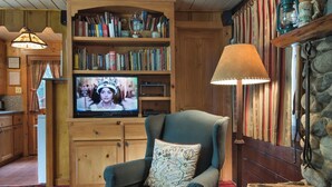A cozy living room with a television, a comfortable armchair, a bookshelf, and a stone fireplace. - Chipmunk Hollow (Yosemite National Park)