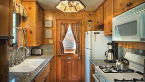 A compact kitchen with wooden cabinets, a granite countertop, a sink, a stove, a microwave, and a window with curtains. - Chipmunk Hollow (Yosemite National Park)