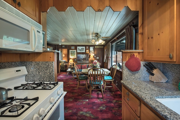 A kitchen with a stove, microwave, granite countertop, and wooden cabinets. - Chipmunk Hollow (Yosemite National Park)