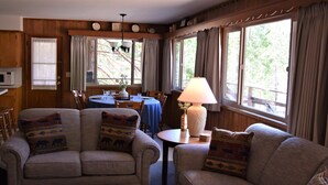 A cozy living room with two sofas and a round coffee table, a dining table with chairs, and large windows with curtains. - Sequoia House (Yosemite National Park)