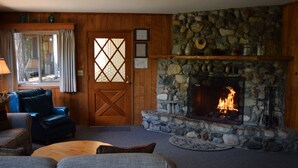 A cozy room with a stone fireplace, wooden walls, a blue leather chair, and a wooden door with a diamond pattern. - Sequoia House (Yosemite National Park)