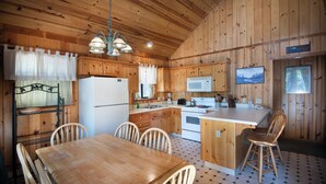 A wooden cabin interior with a dining table, chairs, a kitchen area including a refrigerator, microwave, stove, and a sink. - Wawona Cabin (Yosemite National Park)