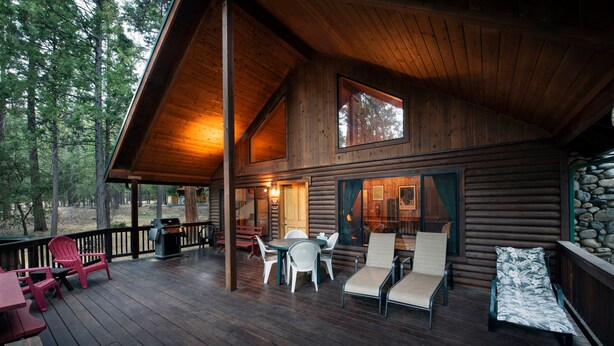 A wooden cabin with a deck, outdoor seating, and a stone wall. - Wawona Cabin (Yosemite National Park)