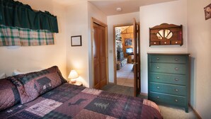 A bedroom with a bed, a dresser, a window with a curtain, and a door leading to another room. - Wawona Cabin (Yosemite National Park)