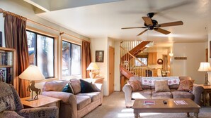 Una sala de estar acogedora con dos sofás, una mesa de centro y un ventilador de techo. Una escalera conduce a otra habitación.