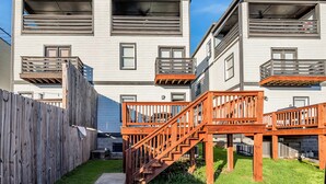 Un moderno edificio residencial de varios pisos con balcones, escaleras de madera y una cerca de madera.