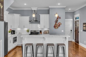 Une cuisine moderne avec des armoires blanches, une cuisinière en acier inoxydable et un îlot central doté de tabourets de bar.