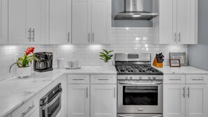 Una cocina moderna con muebles blancos, estufa de acero inoxidable y horno integrado.