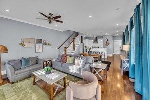 A spacious living area with a sofa, coffee table, and a dining table. A staircase leads to a kitchen area. - Fall Nashville getaway: game room, balcony & backyard, sleeps 12 (Nashville)