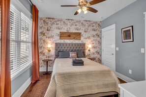 A bedroom with a tufted headboard, a bed with a quilt, two bedside lamps, a ceiling fan, a window with blinds, and a door. - Nashville home with game room, 3 balconies & backyard, sleeps 12 (Nashville)