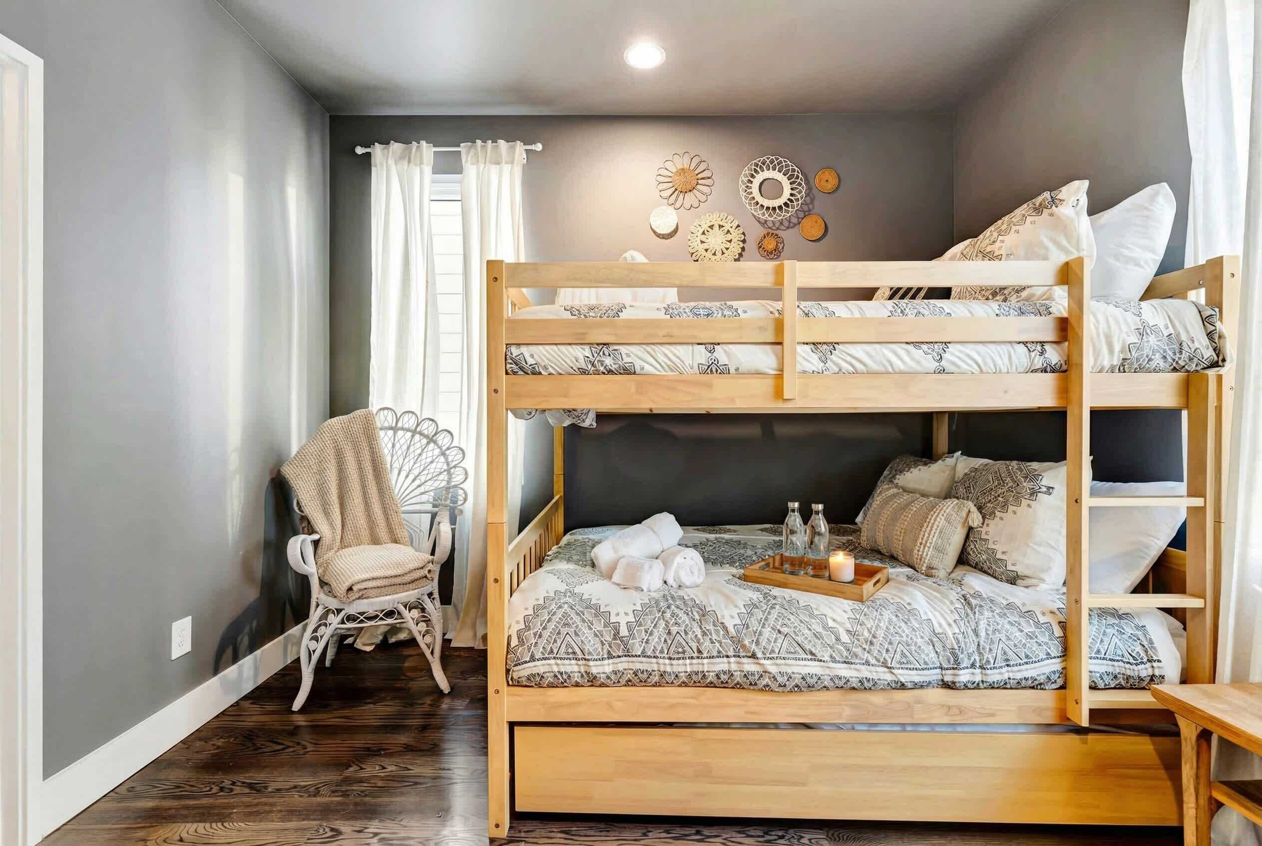 Een stapelbed met gestreken beddengoed, een rieten stoel en decoratieve wandkunst.