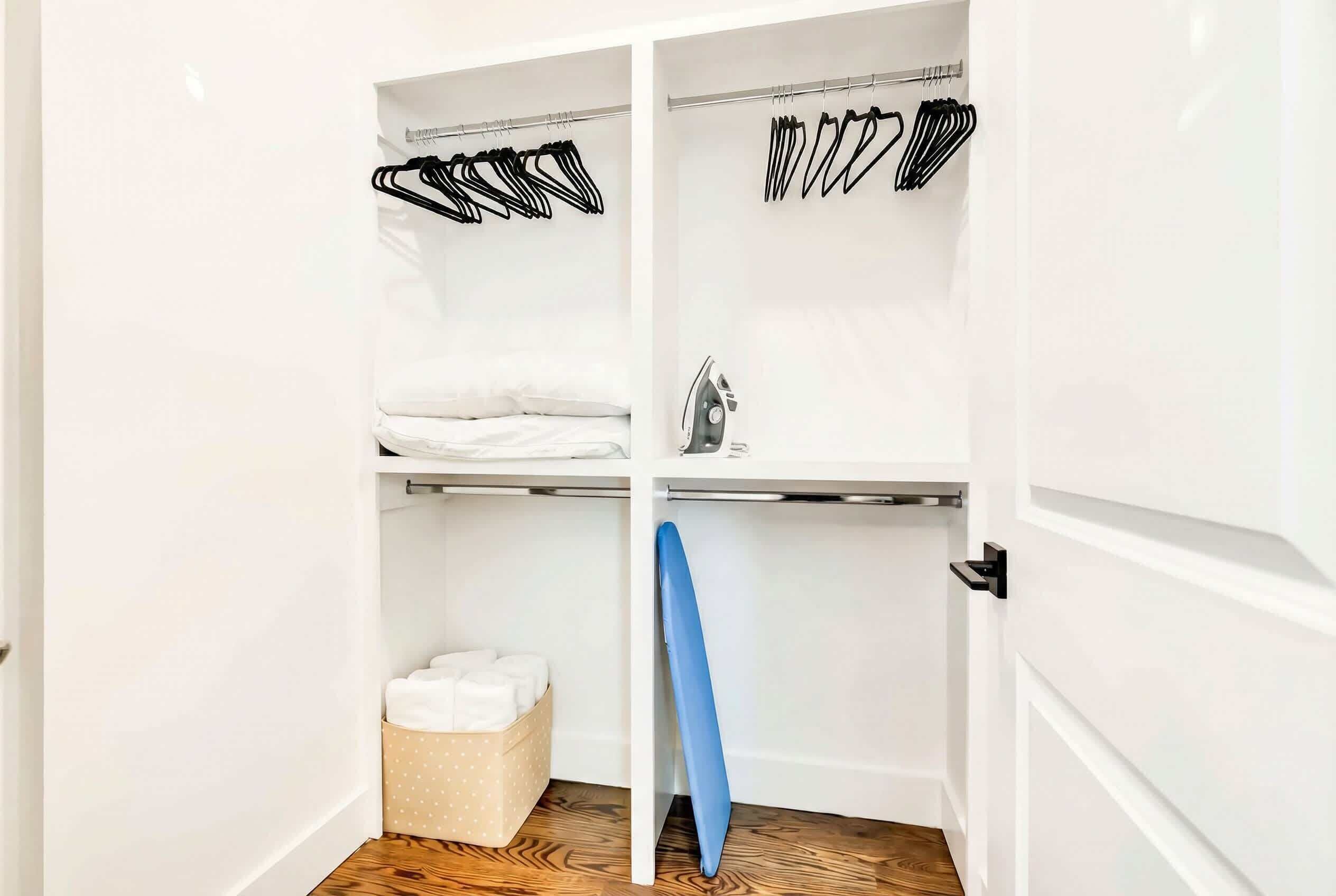 A walk-in closet with multiple shelves, hanging space, and a blue ironing board.