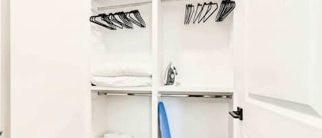 Un vestidor con amplias repisas, espacio para colgar ropa y un tablero de planchar azul.
