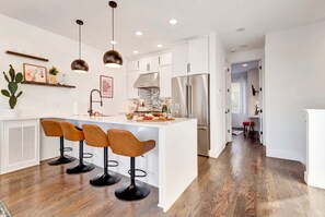 A modern kitchen with a central island, bar stools, pendant lighting, and a stainless steel refrigerator. - Nashville hot tub & karaoke game room home, sleeps 13, 4 bedrooms (Nashville)