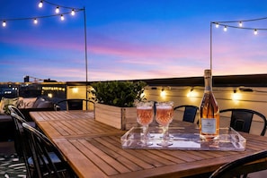 A wooden table with two glasses of champagne and a bottle on a tray, set outdoors with string lights and a cityscape in the background. - Nashville hot tub & karaoke game room home, sleeps 13, 4 bedrooms (Nashville)
