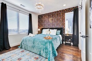 Quarto com uma cama grande, tapete estampado, parede decorativa e um candelabro.
