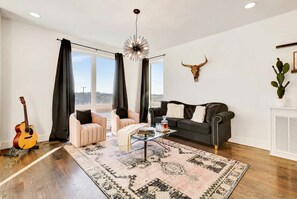 A living room with a sofa, armchair, coffee table, and a guitar. - Nashville bachelorette house with hot tub, karaoke stage & game room, sleeps 13 (Nashville)