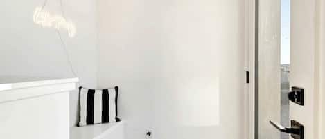 A minimalist room with a white wall, a black and white striped pillow, a white shelf, and a door with a black handle.