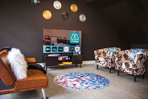 A modern living room with a flat-screen TV displaying a streaming service, a patterned rug, and a sofa with a cow print design. - Nashville hot tub & game room house, sleeps 13 on VRBO (Nashville)