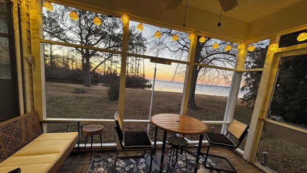 A sunroom with a view of the beach, a wooden table, and a bench.