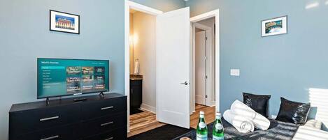 A hotel room with a bed, a TV on a dresser, and a tray with bottles and a candle.
