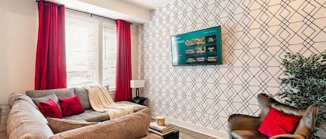 Una sala moderna con un sofá modular, un sillón individual, un televisor de pantalla plana montado en la pared y un papel tapiz estampado.