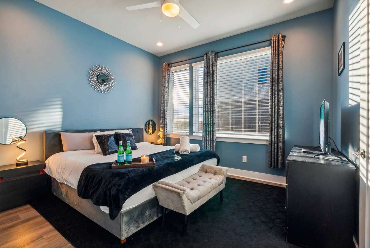 Une chambre à coucher comprenant un lit, une table de chevet, une lampe, une fenêtre avec des rideaux et un téléviseur.
