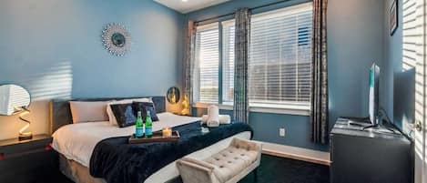A bedroom with a bed, bedside table, lamp, window with curtains, and a television.