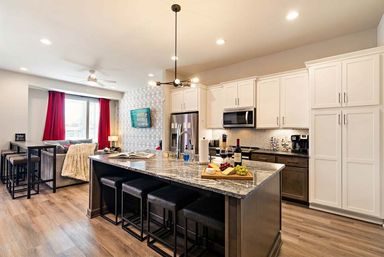 A modern kitchen with a central island, bar stools, stainless steel appliances, and a dining area with a sofa and chairs.