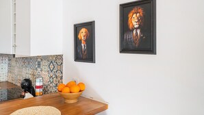 Keittiössä on kahvinkeitin, kulhollinen appelsiineja ja kaksi kehystettyä kuvaa seinällä.