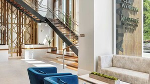 A modern lobby with a reception desk, a staircase, and a seating area with a sofa and armchairs. - Downtown ATL Presidential Suite, Near Benz Stadium (Atlanta)