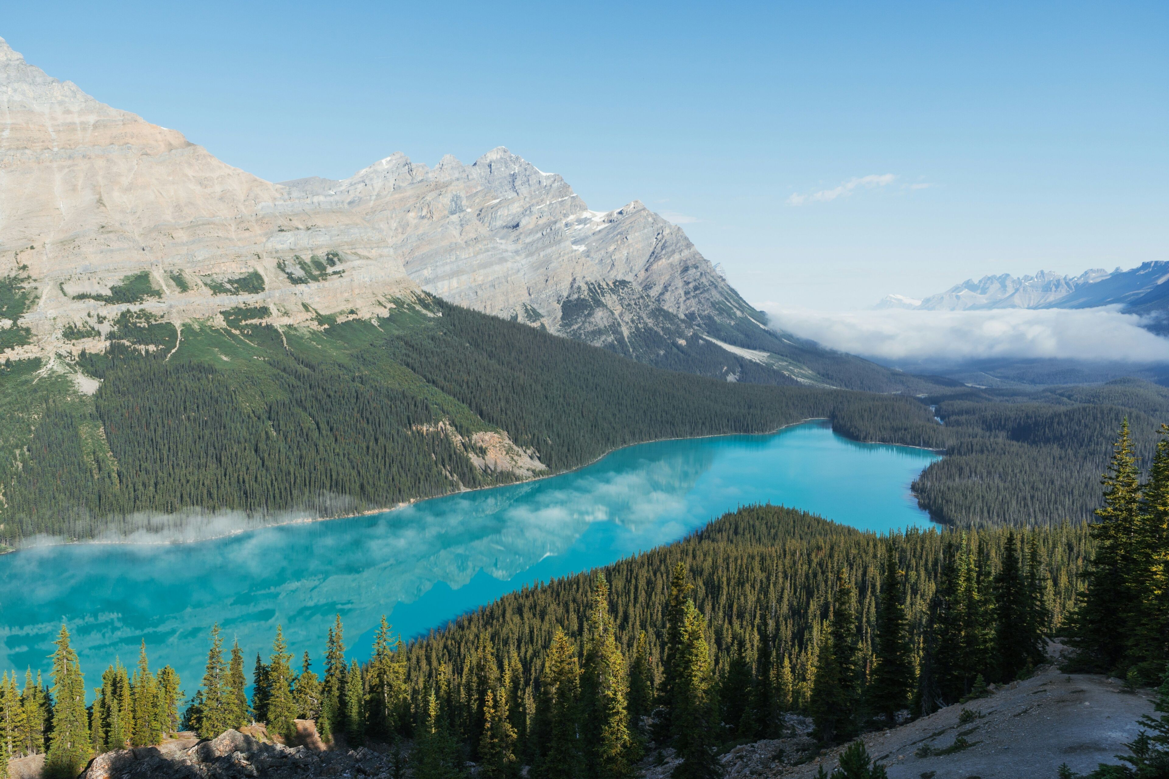 Een bergachtig landschap met een turquoise meer, omringd door dichte bossen en rotsachtig terrein.
