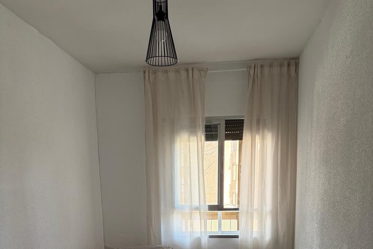 Une chambre à coucher avec un lit, une petite table et une fenêtre avec des rideaux.