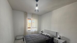 A bedroom with a bed, bedside tables, a heater, and a window with curtains. - ApartaHotel Achicoria (Madrid)