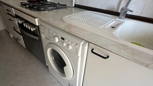 A compact kitchen with a built-in washer and dryer, a gas stove, and a sink. - ApartaHotel Achicoria (Madrid)