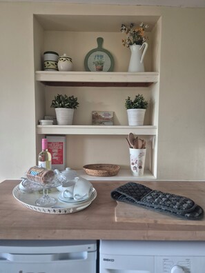 A kitchen counter with a wine bottle, a corkscrew, a tray with glasses, a basket, and a remote control. - Cosy garden cottage style flat with patio views (Grange-over-Sands)