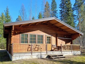 A wooden cabin with a covered porch, large windows, and a concrete foundation.