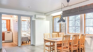 Moderni keittiö, jossa on sisäänrakennettu liesi, ruokailutila puupöydällä ja -tuoleilla sekä suuri ikkuna, jossa on sälekaihtimet.
