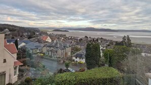 A coastal town with traditional stone houses, a main road, and a view of the sea and distant hills. - Detached house with three flats | Amazing views (Grange-over-Sands)
