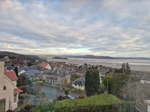 A coastal town with traditional stone houses, a main road, and a view of the sea and distant hills. - Detached house with three flats | Amazing views (Grange-over-Sands)