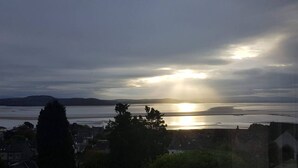 A coastal view with a sunset over water, buildings, and a prominent tree in the foreground. - Detached house with three flats | Amazing views (Grange-over-Sands)