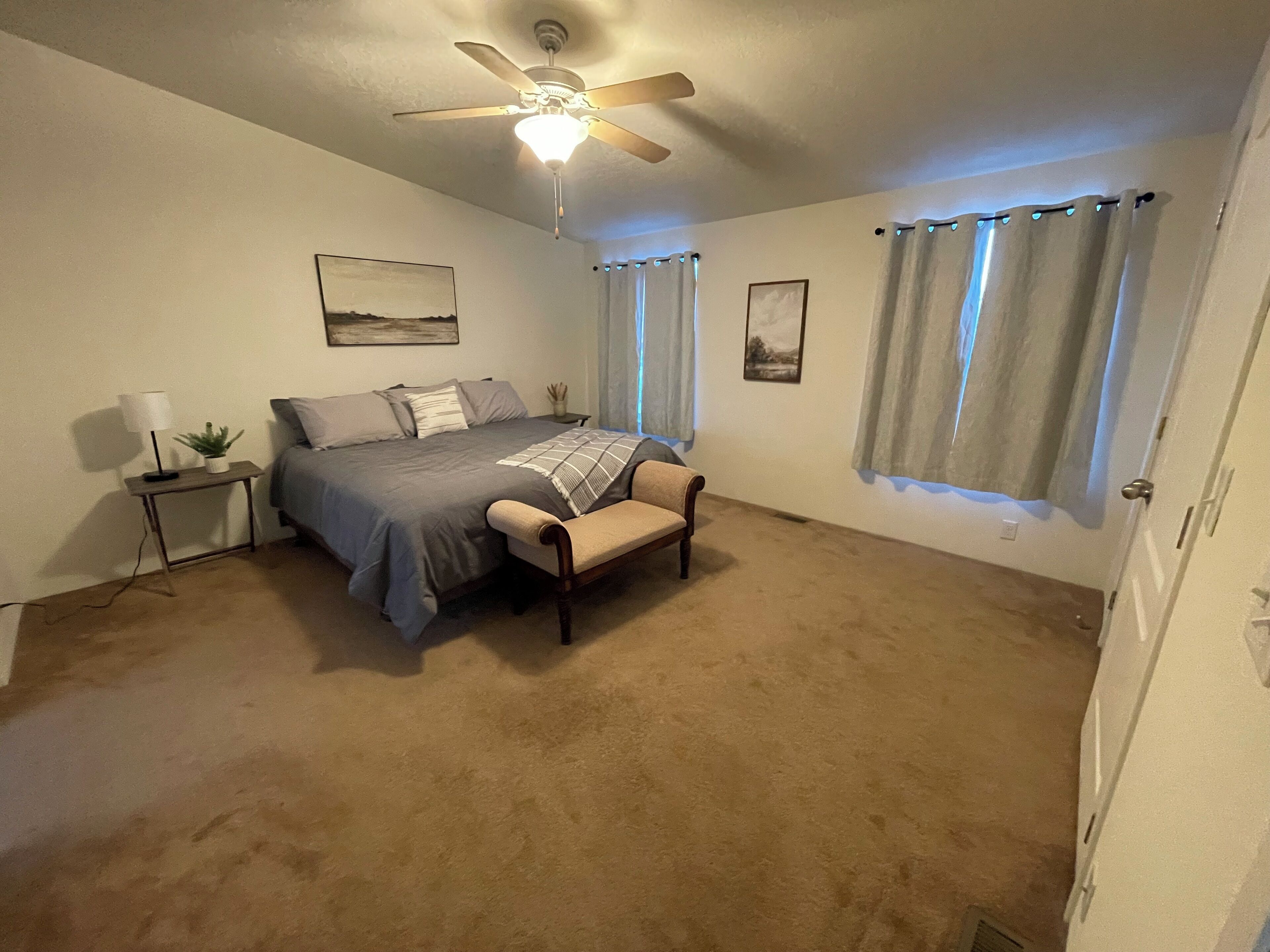 A bedroom with a bed, a chair, a nightstand, a lamp, and a ceiling fan.