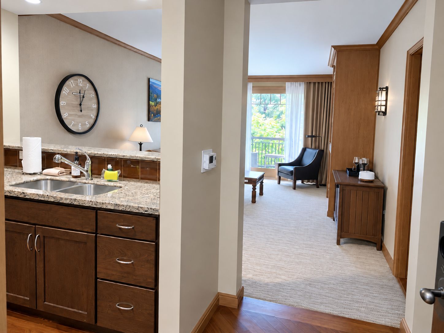 A hotel room with a kitchen area, a dining area, and a balcony with a view.