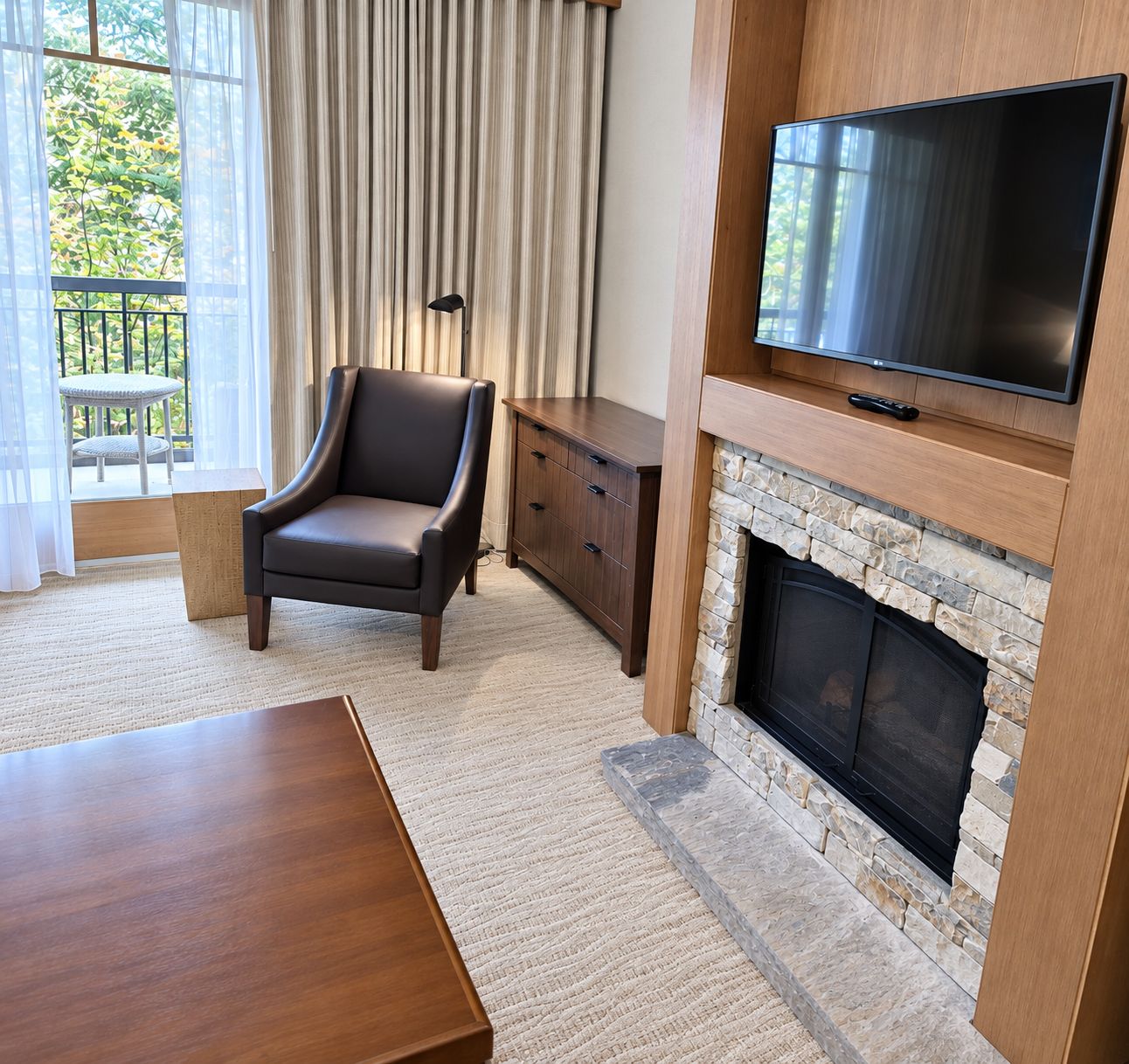 A modern living room with a fireplace, a flat-screen TV, a leather armchair, and a dining table.