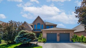Une maison à deux étages avec un garage, une pelouse bien entretenue et de grands arbres.