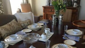 Une table à manger dressée avec des assiettes, des bols et des couverts, entourée d’un canapé et d’un meuble décoratif.