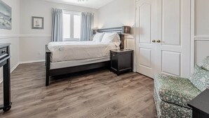 Quarto com cama, mesa de cabeceira, luminária e uma cadeira estampada.