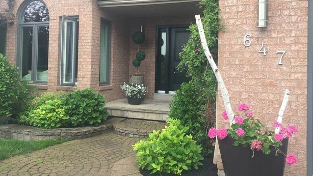 Une maison en briques avec le numéro 647 sur le mur, un porche avec une plante en pot et un petit jardin.